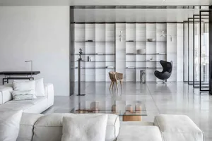 A modern living room with concrete walls, white furniture, and a glass coffee table.