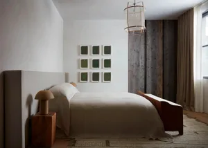A minimalist bedroom with a white bed covered in textured cotton bedding, framed artwork on the wall, and a wooden headboard.