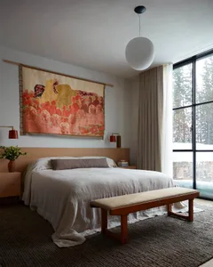 Minimalist bedroom featuring a wooden bed with white bedding, large tapestry, and a wooden bench.