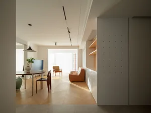 Modern minimalist residential interior featuring a round dining table with a pendant light, an orange leather sofa, and woode