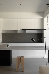 A modern minimalist kitchen with white cabinets, a concrete countertop, and wooden stools.