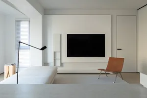 A modern minimalist living room with a white sofa, a brown leather chair, a black adjustable floor lamp, and a large screen T