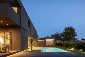 A modern residential home with concrete walls and a glass swimming pool at dusk.