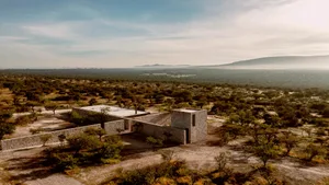 A modern stone house surrounded by trees in a desert landscape.