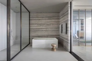 Modern bathroom featuring a freestanding tub, concrete walls, and travertine flooring.