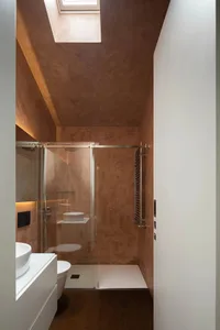 A modern bathroom features a concrete shower enclosure with a glass sliding door, a white floating vanity sink, and a skyligh