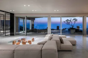 Modern living room with concrete floor and large windows overlooking the sea.