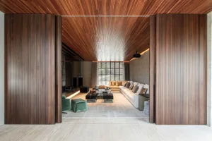 Modern living room with concrete, wood, and glass materials, featuring a lounge area and large windows.