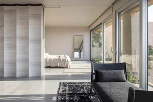 A minimalist bedroom with a concrete wall, glass doors, and a black upholstered bench.