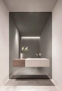 A minimalist bathroom featuring a concrete vanity and wall-mounted sink, illuminated by recessed lighting and adorned with a 