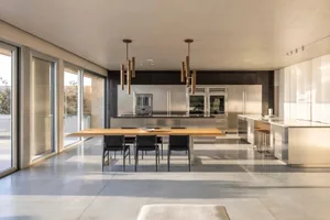 A modern residential kitchen featuring stainless steel cabinets and countertops, with a wooden dining table and black chairs.