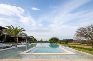 Modern residential outdoor swimming pool with glass walls and lounge chairs.
