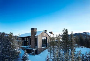 現代鄉村風雪地小屋，搭配覆雪樹木與藍天。