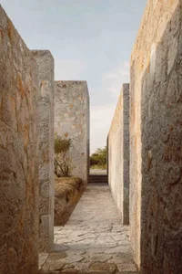 A stone pathway lined with tall stone walls, leading to an entrance.
