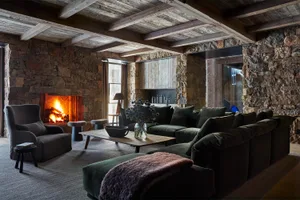 A cozy living room with wooden and stone elements, featuring a comfortable sofa, chairs, and a warm fireplace.