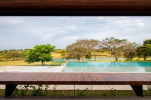 A modern pool with a wooden deck and surrounding greenery, featuring a view of a calm lake and trees.