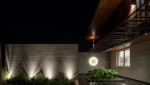 A modern residential architecture featuring concrete walls, illuminated by warm lights, and adorned with green plants in plan