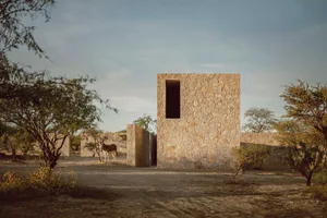 A rustic stone house with a single window in a desert landscape.