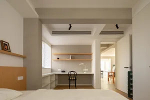 A minimalist bedroom with wooden shelves, a black chair, and a white desk.