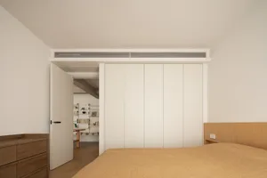 Modern minimalist bedroom with white walls, wooden floor, and a walnut wood headboard on a bed with a yellow blanket.