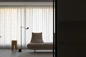 Modern minimalist living room with a beige upholstered lounge chair, a black floor lamp, and sheer white curtains.