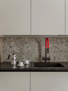 A sleek modern kitchen featuring a black terrazzo countertop with a black and red faucet, white espresso cups, and a silver e