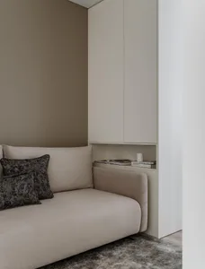 A modern minimalist living room with a beige sectional sofa adorned with patterned cushions, situated against a light-colored