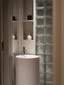 A minimalist bathroom with a glass-brick wall and a round pedestal sink.