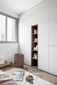 Minimalist bedroom with white walls, wooden furniture, and a large window allowing natural light to enter.