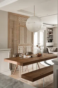 A minimalist dining room with a wooden table, chairs, and bench, featuring a white pendant light and a bookshelf.