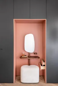 Minimalist vanity area with a white stool, pink walls, and a white shelf holding a perfume bottle and a brush.