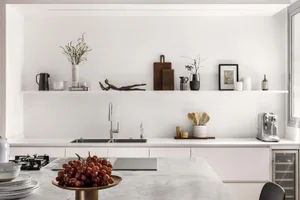 Modern minimalist kitchen featuring white marble countertops and white cabinets, with decorative items on shelves.