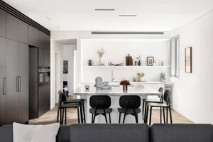 A modern kitchen featuring a black marble island with black chairs and wooden flooring, surrounded by white walls and black c