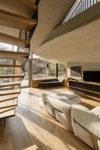 A modern living room with wood stairs, large windows, and a cozy sofa.