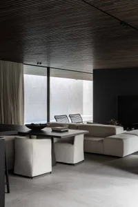 A modern minimalist living room with a concrete floor, a large window, white sofas, and a dining table.