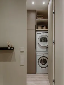 A modern, neutral-colored laundry room with stacked washer and dryer appliances.