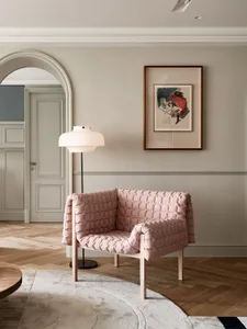 A modern living room featuring a pink upholstered armchair, a wooden floor, and a framed artwork on the wall.