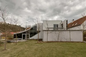 A contemporary residential home featuring modern architecture, concrete walls, glass windows, and a sloping green roof.