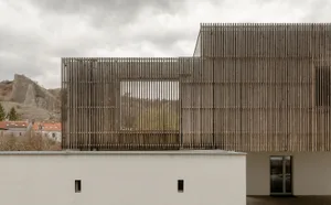 A modern wooden building with a slatted facade overlooking a natural landscape.