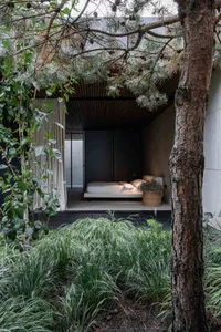 Modern minimalist bedroom with a wooden canopy over a bed, surrounded by greenery.