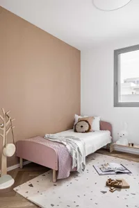 A minimalistic children's room featuring a wooden bed with a lion-shaped pillow and a patterned rug.