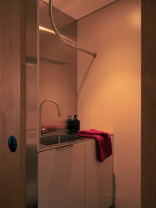A minimalist laundry room with a matte metal sink, towel, and surrounding cabinetry.