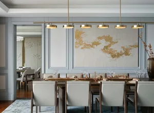 A modern dining room with a large table, chairs, and decorative wall art featuring gold patterns on a light background.