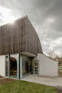 A modern house featuring a concrete exterior with a wooden roof and large glass windows.
