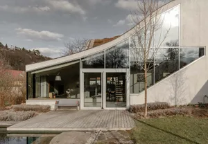 A modern house exterior featuring glass walls and concrete materials.