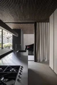 A modern minimalist kitchen with a wood-paneled ceiling and concrete countertops.