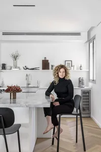 A minimalist kitchen featuring a marble countertop with a woman sitting on a stool.