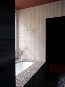 Modern bathroom with a white terrazzo tub surrounded by pink and white checkered tile walls and a black counter