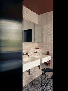 Modern bathroom with white and red tiled walls, white countertops, and black metal stool with a terrazzo floor.