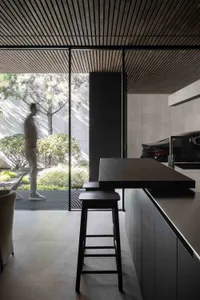 A modern kitchen with a wooden island counter, large windows, and a black stool.